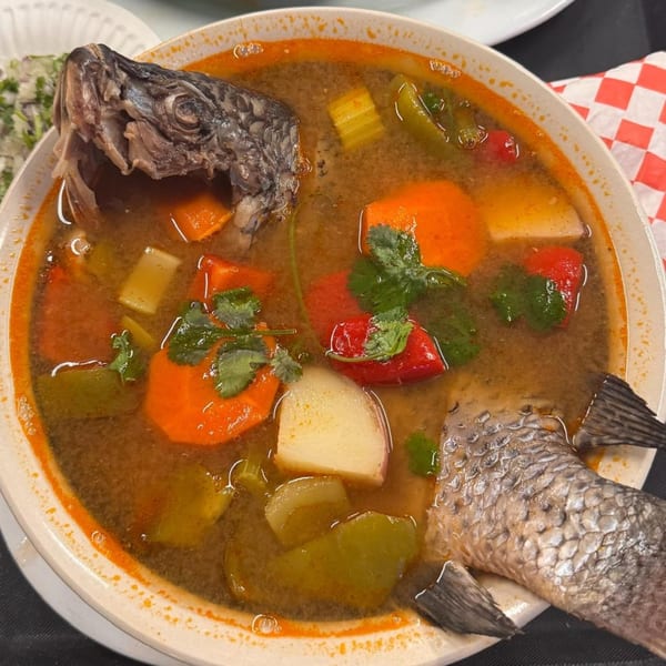 Mexican fish soup with whole fish head and tail, vegetables, and cilantro in a white bowl.