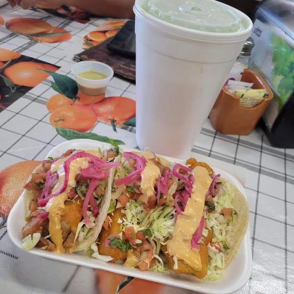Three fish tacos with cabbage, pico de gallo, pink pickled onions, and creamy sauce on a checkered table.